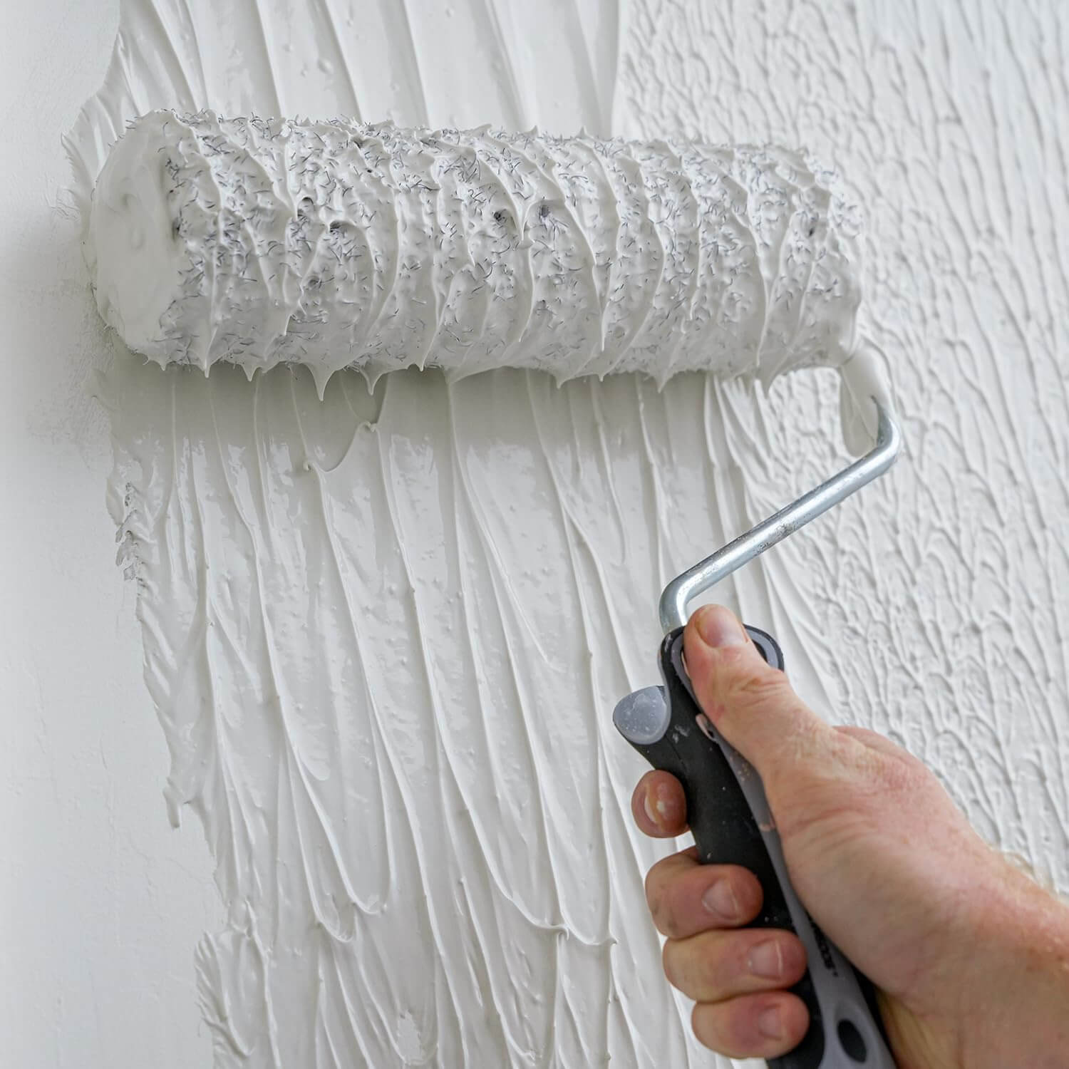 Drywall compound roller cover in use applying mud smoothly on wall surface