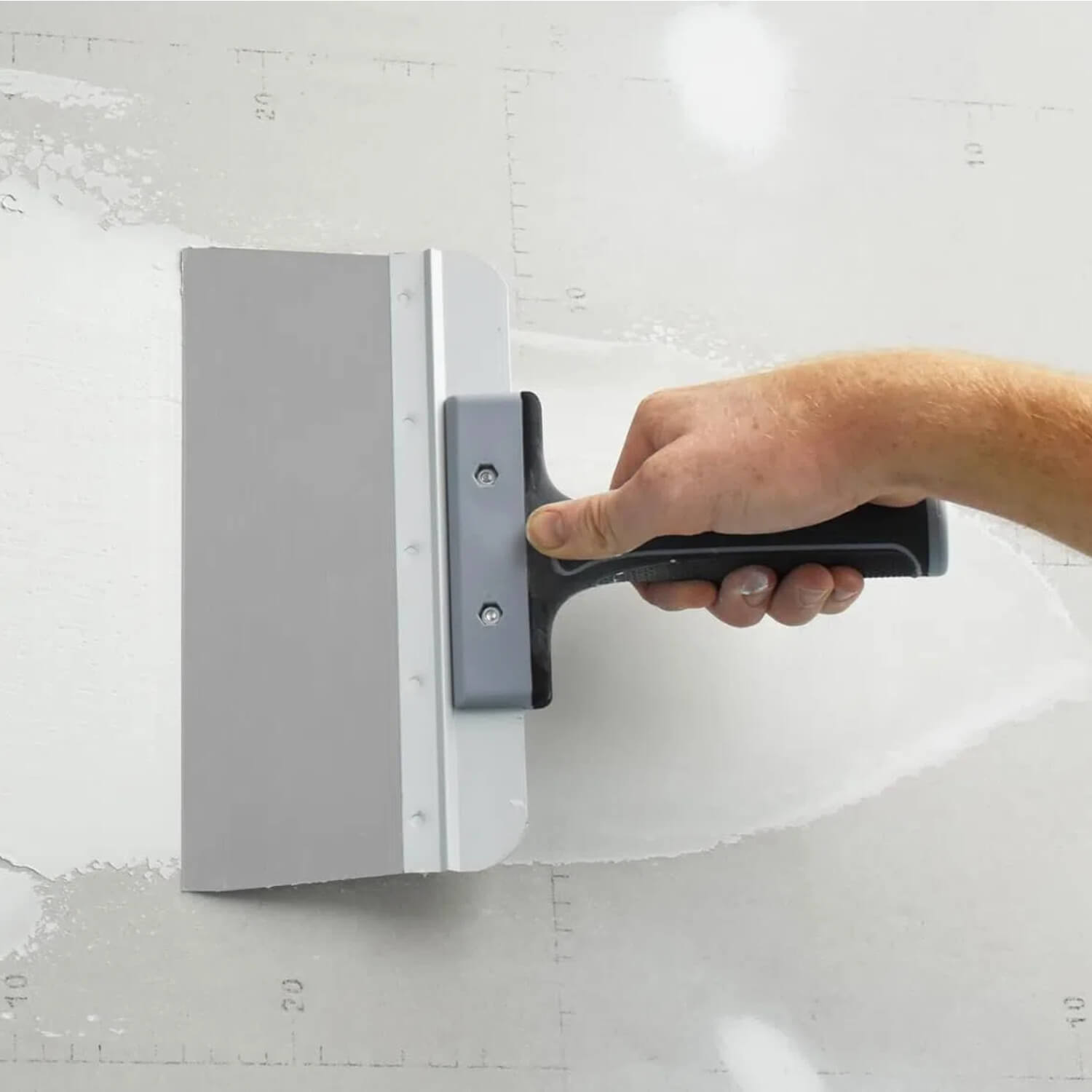 Drywall taping knife in use spreading compound smoothly on wall surface for professional finishing