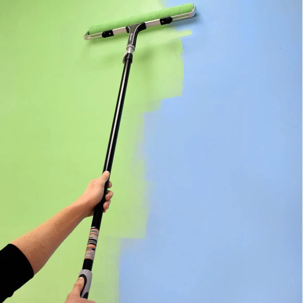 DIY painter using 18 inch paint roller with extension pole to paint high walls easily